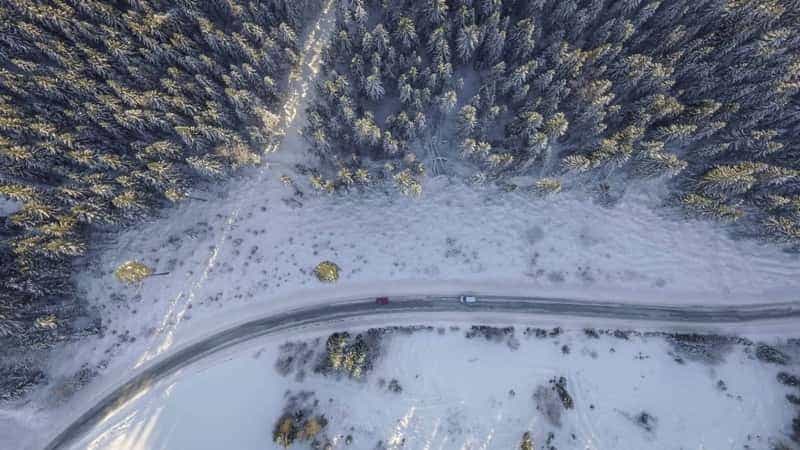 Luftaufnahme einer geräumten Straße durch einen verschneiten Wald
