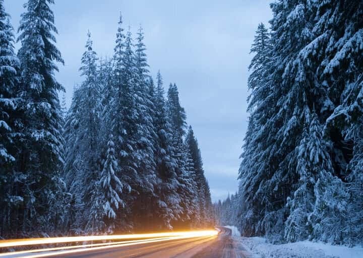 Langzeitbelichtung einer winterlichen Waldstraße bei Dämmerung mit Lichtspuren eines Fahrzeugs